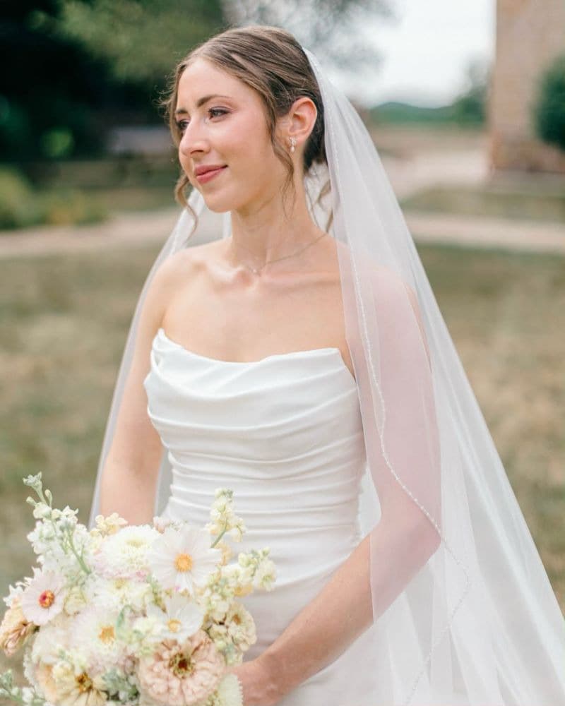 Bride in a long veil looking off to the side, holding a soft garden bouquet