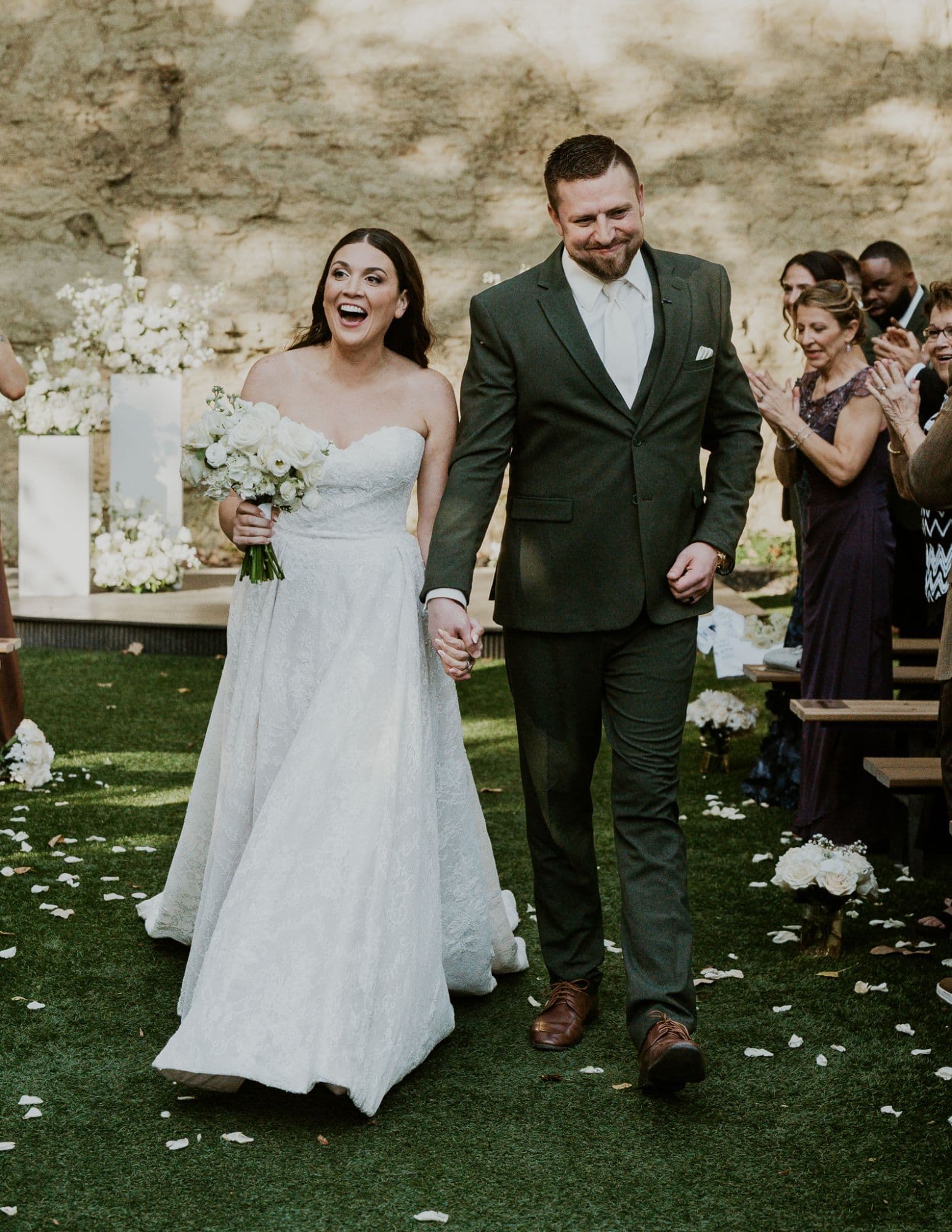 Newlyweds walking the aisle holding hands as guests applaud